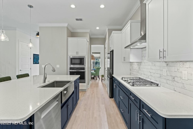 kitchen with blue cabinets, stainless steel appliances, a sink, visible vents, and wall chimney exhaust hood