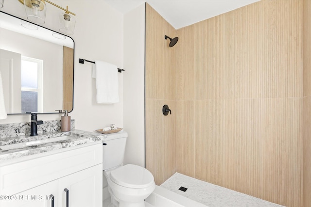 bathroom with tiled shower, vanity, and toilet