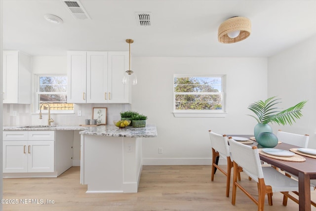 kitchen with pendant lighting, white cabinets, a sink, and visible vents