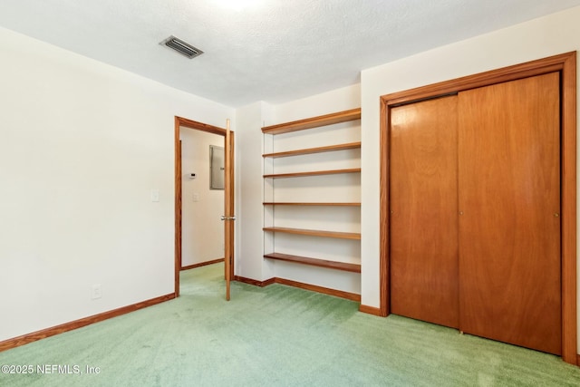 unfurnished bedroom with a textured ceiling, carpet floors, visible vents, baseboards, and electric panel