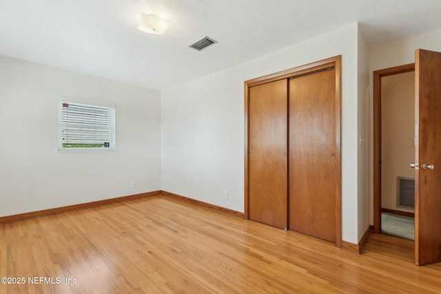 unfurnished bedroom featuring baseboards, a closet, visible vents, and light wood-style floors