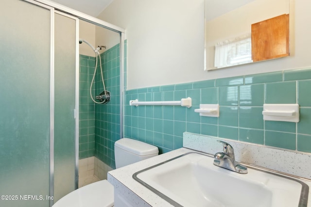 full bathroom featuring a wainscoted wall, tile walls, toilet, a shower stall, and vanity