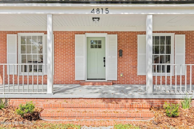 property entrance featuring a porch and brick siding