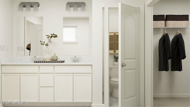 full bathroom featuring toilet, a sink, baseboards, a spacious closet, and double vanity