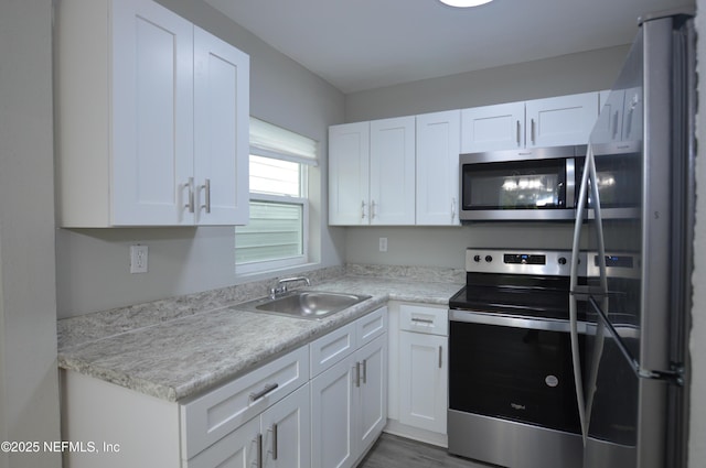 kitchen featuring stainless steel appliances, wood finished floors, a sink, and white cabinetry