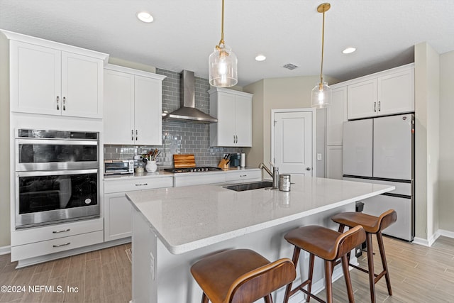 kitchen with stainless steel appliances, a sink, visible vents, wall chimney range hood, and backsplash