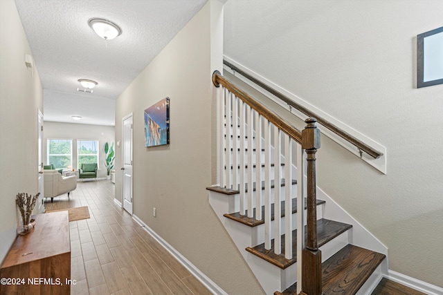 stairway with visible vents, a textured ceiling, baseboards, and wood finished floors