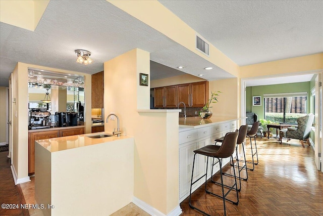 kitchen with visible vents, a kitchen breakfast bar, a peninsula, a textured ceiling, and a sink