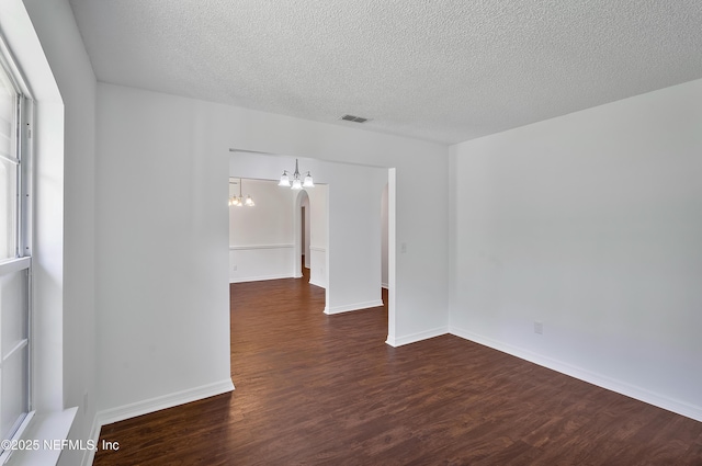 spare room featuring a chandelier, visible vents, a textured ceiling, and dark wood-type flooring