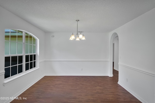 empty room featuring baseboards, arched walkways, dark wood-style floors, an inviting chandelier, and a textured ceiling