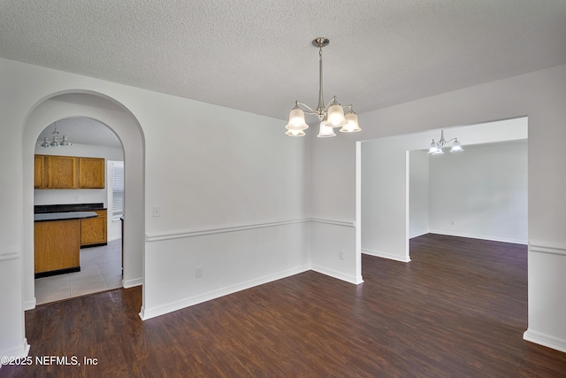 spare room with baseboards, arched walkways, dark wood finished floors, a textured ceiling, and a chandelier