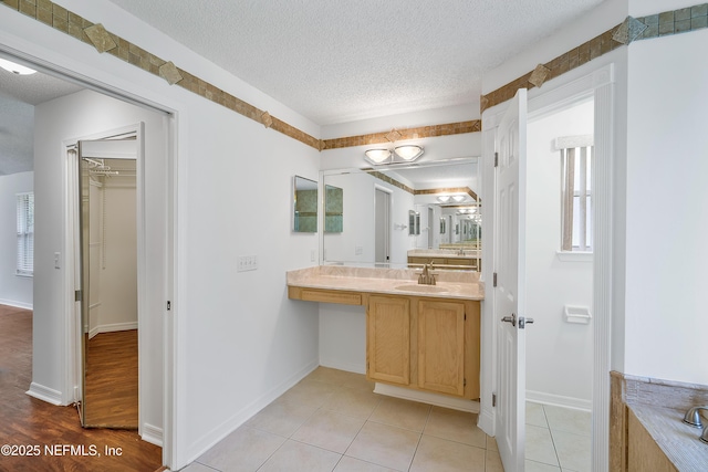 bathroom with a textured ceiling, tile patterned flooring, vanity, and baseboards