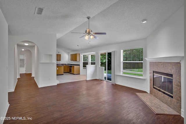 unfurnished living room featuring lofted ceiling, a tile fireplace, visible vents, and light wood-style floors