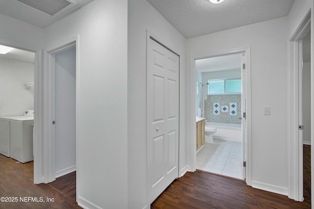 hallway featuring a textured ceiling, visible vents, dark wood-style flooring, and washer and dryer