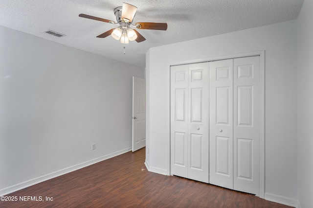 unfurnished bedroom featuring a textured ceiling, dark wood-type flooring, visible vents, baseboards, and a closet