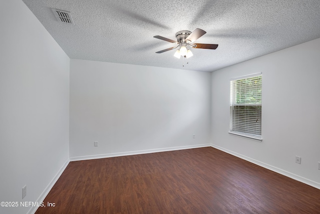 empty room with dark wood-style floors, baseboards, visible vents, and a ceiling fan