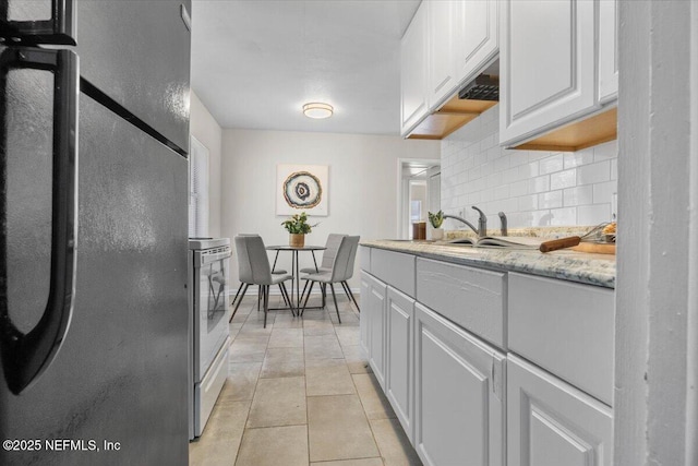 kitchen with light tile patterned floors, decorative backsplash, freestanding refrigerator, white cabinetry, and a sink