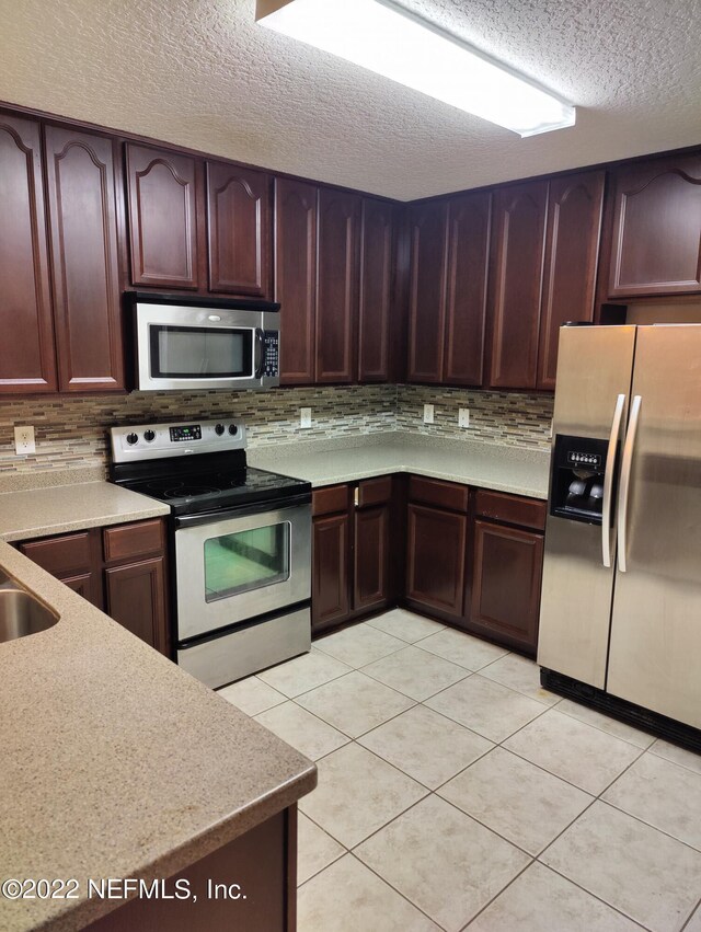 kitchen with light tile patterned floors, tasteful backsplash, stainless steel appliances, a textured ceiling, and light countertops