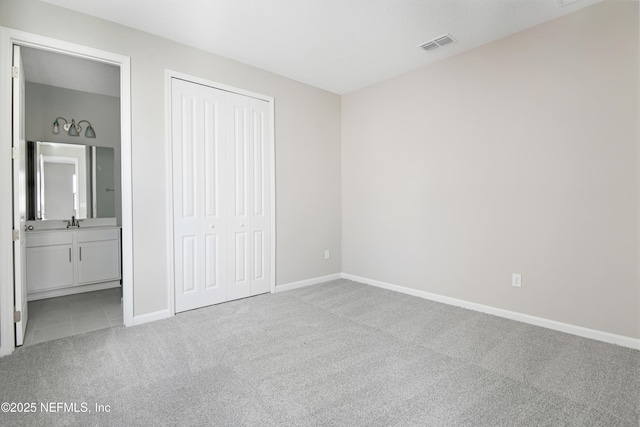 unfurnished bedroom with a closet, visible vents, light carpet, a sink, and baseboards