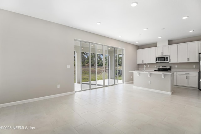 kitchen featuring a breakfast bar area, white cabinets, light countertops, appliances with stainless steel finishes, and an island with sink