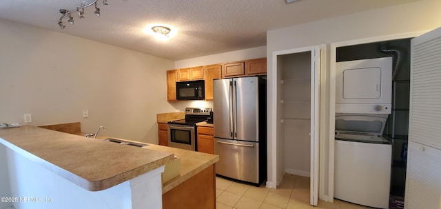 kitchen with a peninsula, a sink, stainless steel appliances, and stacked washer / dryer