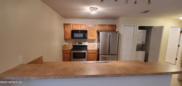 kitchen featuring visible vents, appliances with stainless steel finishes, stacked washer / drying machine, a peninsula, and a sink