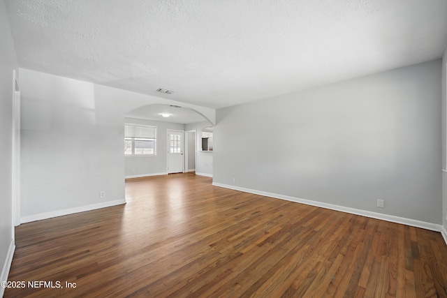 unfurnished living room featuring arched walkways, a textured ceiling, wood finished floors, visible vents, and baseboards