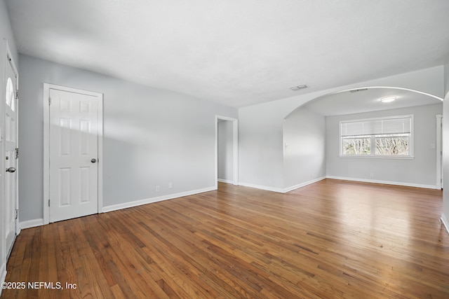 empty room with arched walkways, wood finished floors, visible vents, and baseboards