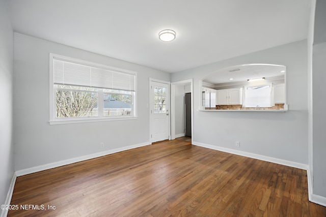 empty room with baseboards, arched walkways, and wood finished floors