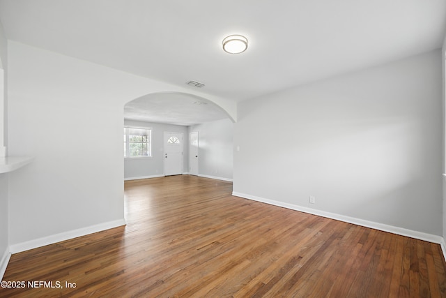 spare room with wood-type flooring, visible vents, arched walkways, and baseboards