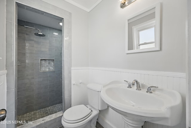 bathroom with toilet, ornamental molding, a stall shower, wainscoting, and a sink