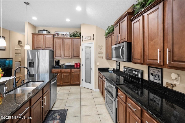 kitchen with pendant lighting, stainless steel appliances, light tile patterned flooring, a sink, and dark stone countertops