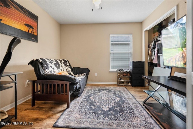 living area with a textured ceiling, baseboards, and wood finished floors