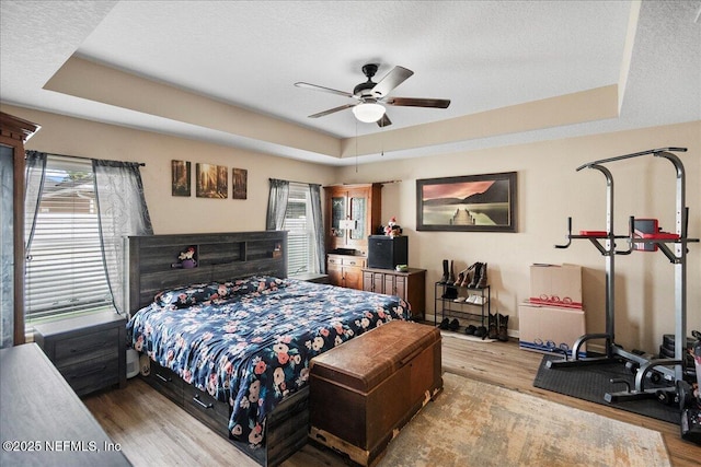 bedroom featuring a textured ceiling, baseboards, a raised ceiling, and wood finished floors