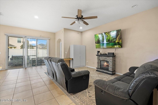 living room with baseboards, a ceiling fan, light tile patterned flooring, a stone fireplace, and recessed lighting