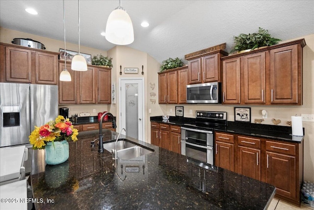 kitchen with hanging light fixtures, a kitchen island with sink, vaulted ceiling, stainless steel appliances, and a sink