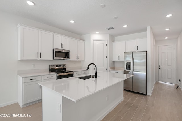 kitchen featuring a center island with sink, appliances with stainless steel finishes, light countertops, white cabinetry, and a sink