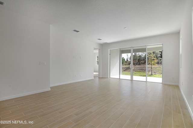 unfurnished room with a textured ceiling, light wood-style flooring, and baseboards