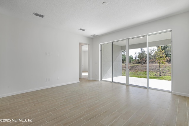 empty room with light wood finished floors, baseboards, visible vents, and a textured ceiling