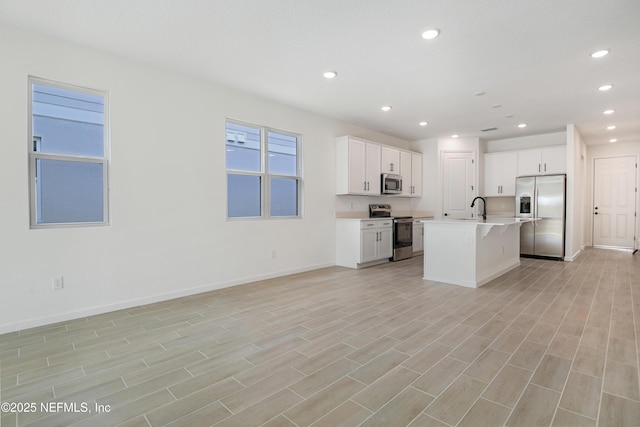 kitchen featuring a center island with sink, light countertops, appliances with stainless steel finishes, white cabinets, and a sink