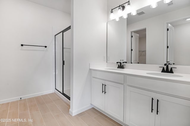 full bathroom featuring double vanity, a stall shower, baseboards, and a sink