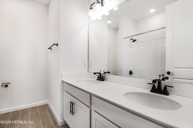 bathroom featuring double vanity, baseboards, a tile shower, and a sink