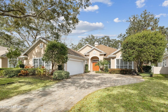 view of front facade featuring decorative driveway, a chimney, stucco siding, a front yard, and a garage