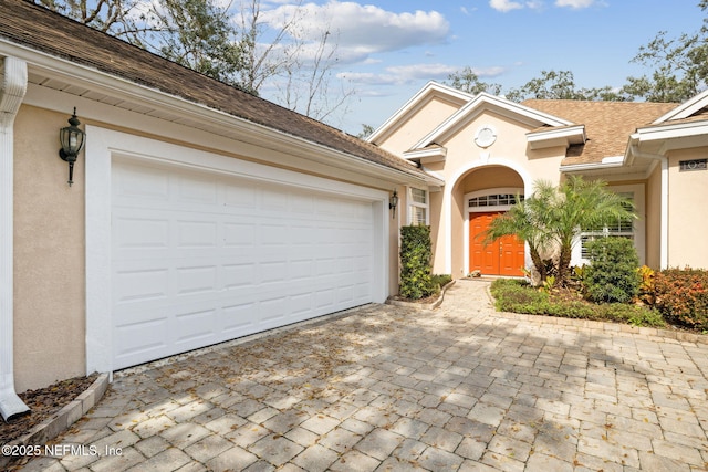 view of front of house with roof with shingles, decorative driveway, and stucco siding