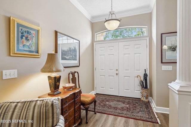 foyer entrance featuring baseboards, wood finished floors, decorative columns, and crown molding