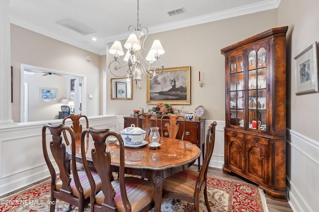 dining space with visible vents, a wainscoted wall, ornamental molding, wood finished floors, and a notable chandelier