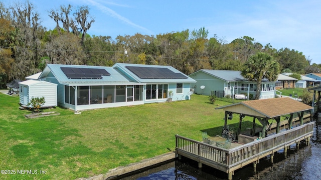 back of property with a water view, a sunroom, roof mounted solar panels, and a lawn