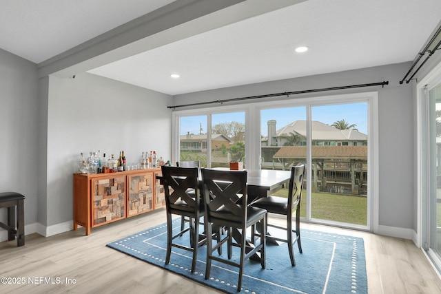dining space with a bar, light wood-type flooring, recessed lighting, and baseboards