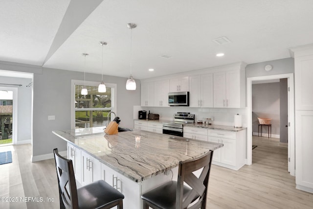 kitchen with light wood-style flooring, a kitchen breakfast bar, white cabinets, appliances with stainless steel finishes, and decorative backsplash