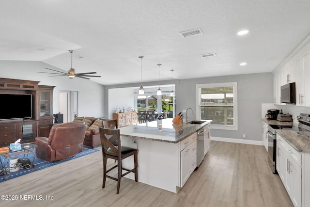 kitchen with a breakfast bar, light wood finished floors, stainless steel appliances, white cabinetry, and a sink